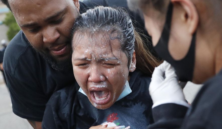 A woman is helped after being hit with pepper spray after curfew on Sunday, May 31, 2020, in Minneapolis. Protests continued following the death of George Floyd, who died after being restrained by Minneapolis police officers on Memorial Day. (AP Photo/John Minchillo)