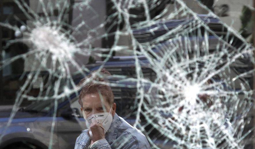 A woman wearing a mask due to coronavirus concerns, looks at a smashed storefront window in Boston&#x27;s Downtown Crossing, Monday, June1, 2020. A march in Boston Sunday to protest the death of George Floyd, who died after being restrained by Minneapolis police officers on May 25, turned violent after dark. (AP Photo/Elise Amendola)