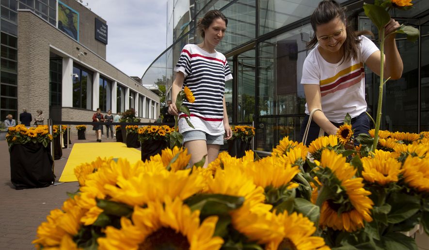Visitors leaving the reopened Van Gogh Museum were offered a free sunflower in Amsterdam, Netherlands, Monday, June 1, 2020. The Dutch government took a major step to relax the coronavirus lockdown, with bars, restaurants, cinemas and museums reopening under strict conditions. (AP Photo/Peter Dejong)