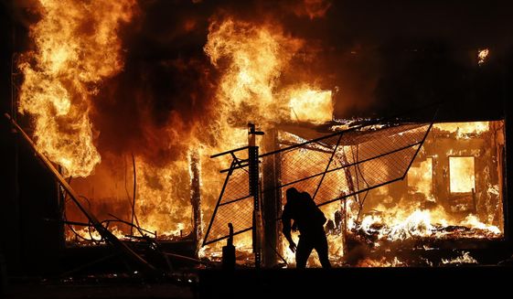 An arsonist adds materials to a fire of a building that once housed a check cashing business, in St. Paul, Minnesota, May 30, 2020. The destruction caused by vandals and looters in cities across the country, who struck as demonstrators took to the streets in reaction to the killing of George Floyd in Minneapolis, has devastated small businesses already reeling from the coronavirus outbreak. (AP Photo/John Minchillo)  ** FILE ** 