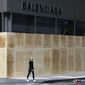 A woman walks by a boarded-up Balenciaga store, Tuesday, June 2, 2020, on Madison Avenue in New York. Protesters broke the window Monday night in reaction to the death of George Floyd, a Black man who died after being restrained by Minneapolis police officers on May 25, 2020. (AP Photo/Mark Lennihan) ** FILE **