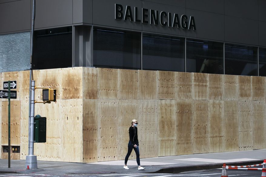 A woman walks by a boarded-up Balenciaga store, Tuesday, June 2, 2020, on Madison Avenue in New York. Protesters broke the window Monday night in reaction to the death of George Floyd, a Black man who died after being restrained by Minneapolis police officers on May 25, 2020. (AP Photo/Mark Lennihan) ** FILE **