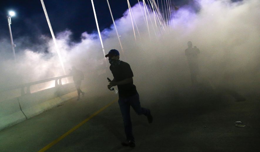 In this Monday, June 1, 2020, photo, a man moves through smoke and tear gas as protesters  marched onto the Margaret Hunt Hill Bridge while demonstrating against police brutality in Dallas. Protests continue over the death of George Floyd, a black man who died after being restrained by Minneapolis police officers on May 25. (Ryan Michalesko/The Dallas Morning News via AP)