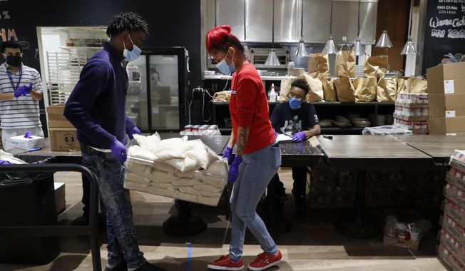 Marquel Gray, center left, and Gaby Torres, center right, carry bags filled with rice as Angel Coronado, left rear, and De&#x27; Monica Dean, right rear, prepare to help add them to box meal kits at Cafe Momentum in Dallas, Wednesday, May 13, 2020. Chef Chad Houser opened the cafe five years ago to help give teens coming out of juvenile detention stability and a push toward success. (AP Photo/Tony Gutierrez)