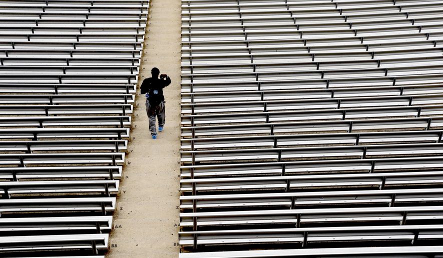 FILE - In this July 16, 2014, file photo, a student walks through empty seats inside Kenan Stadium at the University of North Carolina in Chapel Hill, N.C., where preparations continue for the upcoming college football season. The crippling grip the coronavirus pandemic has had on the sports world has forced universities, leagues and franchises to evaluate how they might someday welcome back fans. (AP Photo/Gerry Broome, File)