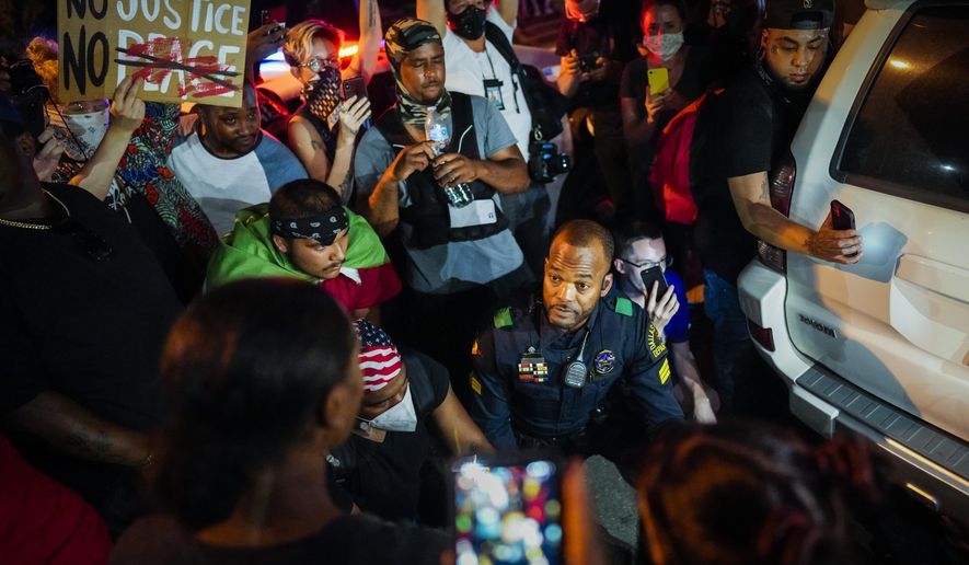 A Dallas police officer stops and gets out of his car to talk and take photos with a group of demonstrators gathered at Lake Cliff Park as protests continue after the death of George Floyd on Tuesday, June 2, 2020, in Dallas. Because of the city-imposed 7:00 p.m. curfew, the group moved from Dallas City Hall to outside the curfew zone in Oak Cliff. (Smiley N. Pool/The Dallas Morning News via AP)