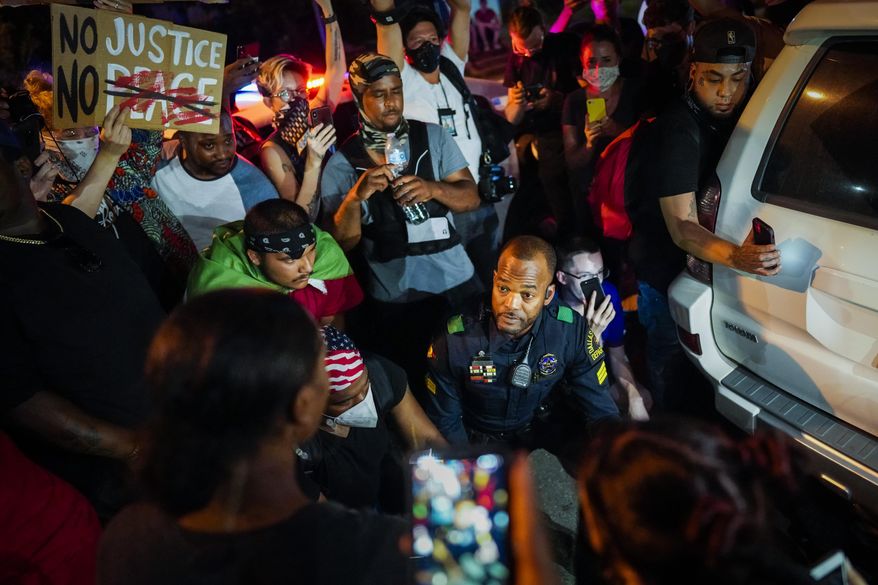 A Dallas police officer stops and gets out of his car to talk and take photos with a group of demonstrators gathered at Lake Cliff Park as protests continue after the death of George Floyd on Tuesday, June 2, 2020, in Dallas. Because of the city-imposed 7:00 p.m. curfew, the group moved from Dallas City Hall to outside the curfew zone in Oak Cliff. (Smiley N. Pool/The Dallas Morning News via AP)