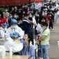 FILE - In this May 15, 2020 file photo, people line up for medical workers to take swabs for the coronavirus test at a large factory in Wuhan in central China&#39;s Hubei province. The Chinese city of Wuhan has tested nearly 10-million people for the new coronavirus in an unprecedented 19-day campaign to check an entire city. (Chinatopix Via AP)