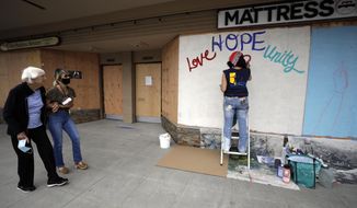 Artist Karla Burner, right, paints a mural on plywood covering the shattered window of a mattress store that was damaged during protests over the death of George Floyd in Minneapolis, Thursday, June 4, 2020, in La Mesa, Calif. California authorities are praising thousands of peaceful protesters who have thronged streets but they also have filed criminal charges against more than 100 people accused of looting and violence. (AP Photo/Gregory Bull)