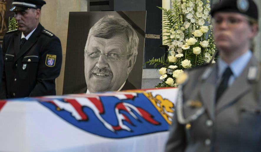 FILE-In this June 13, 2019 file photo a picture of Walter Luebcke stands behind his coffin during the funeral service in Kassel, Germany. German investigators have carried out raids on dozens of people suspected of posting hate messages about a regional politician from Chancellor Angela Merkel’s party who was killed last year. Walter Luebcke, who led the regional administration in the central Kassel region, was shot on June 1, 2019. (Swen Pfoertner/dpa via AP, file)