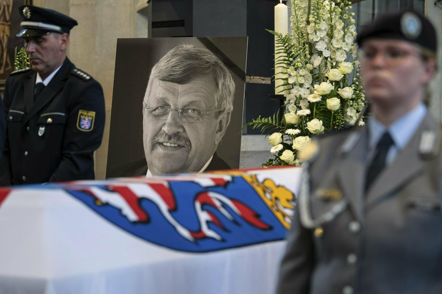 FILE-In this June 13, 2019 file photo a picture of Walter Luebcke stands behind his coffin during the funeral service in Kassel, Germany. German investigators have carried out raids on dozens of people suspected of posting hate messages about a regional politician from Chancellor Angela Merkel’s party who was killed last year. Walter Luebcke, who led the regional administration in the central Kassel region, was shot on June 1, 2019. (Swen Pfoertner/dpa via AP, file)