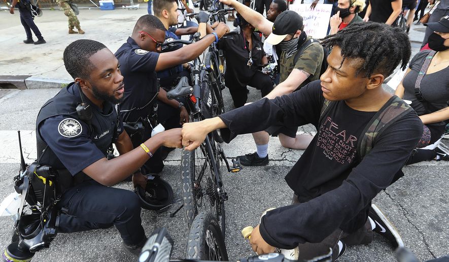 FILE - In this June 3, 2020, file photo, Atlanta Police Officer J. Coleman, left, and protester Elijah Raffington, of Sandy Springs, fist bump in a symbolic gesture of solidarity outside the CNN Center at Olympic Park, in Atlanta. George Floyd, a black man, died after being restrained by Minneapolis police officers on May 25 and his death sparked protests. Black officers find themselves torn between two worlds when it comes to the protests against police brutality happening around the U.S. (Curtis Compton/Atlanta Journal-Constitution via AP, File)