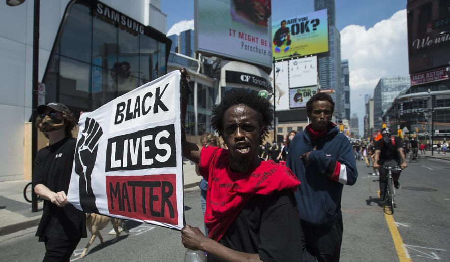 People hold up a Black Lives Matter sign as thousands of people protest at an anti-racism demonstration, in Toronto on Friday, June 5, 2020. George Floyd, a black man, died after he was restrained by Minneapolis police officers on May 25. His death has ignited protests in the U.S. and worldwide over racial injustice and police brutality. (Nathan Denette/The Canadian Press via AP)