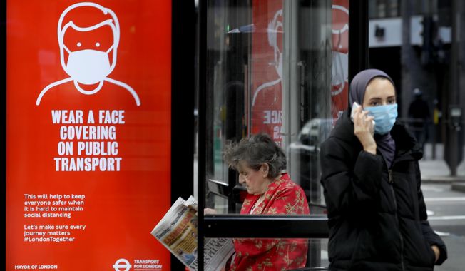 Passengers wait at a bus stop with a sign advising travellers to wear a face covering whilst travelling, in London, Friday, June 5, 2020. It will become compulsory to wear face coverings whilst using public transport in England from Monday June 15. (AP Photo/Kirsty Wigglesworth)