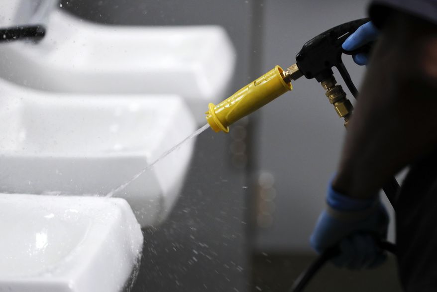 FILE - In this Thursday, March 19, 2020, file photo, a public school employee sanitizes a sink in a bathroom at a U.S. high school. Jobs with state and city governments are usually a source of stability in the U.S. economy, but the financial devastation wrought by the coronavirus pandemic has forced cuts that will reduce public services, from schools to trash pickup. (AP Photo/Charlie Neibergall, File)