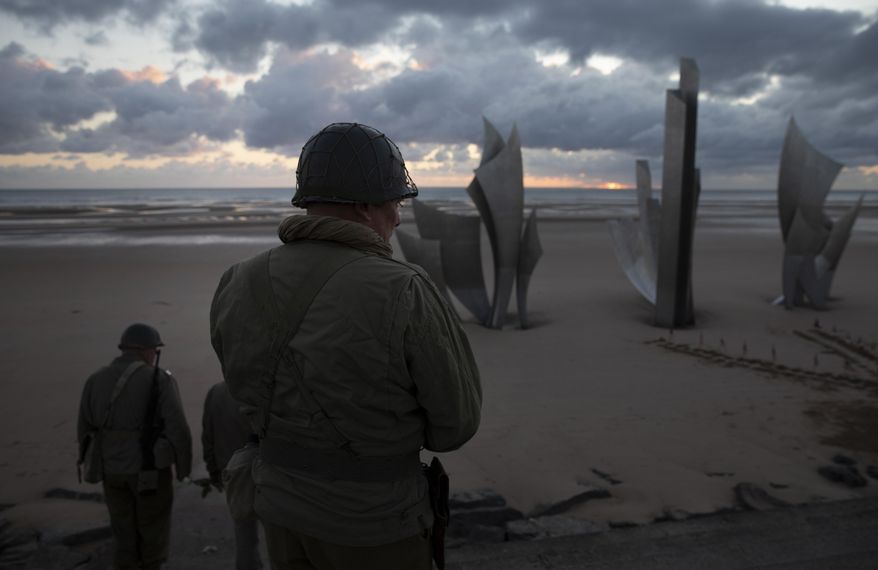 Two men in vintage US WWII uniforms walk toward the Les Braves monument at sunrise prior to a D-Day 76th anniversary ceremony in Saint Laurent sur Mer, Normandy, France, Saturday, June 6, 2020. Due to coronavirus measures many ceremonies and memorials have been cancelled in the region with the exception of very small gatherings. (AP Photo/Virginia Mayo)