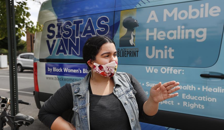 Sistas Van driver Denise Rodriguez pauses in front of the van she uses to pick up and drop off supplies for those in need of help amid the coronavirus outbreak, Tuesday, May 19, 2020, in New York. Originally launched to help survivors of sexual and reproductive violence and physical abuse, the women's network and their van have been delivering badly-needed resources to black and Hispanic communities, which have been disproportionately affected by the fast-spreading virus. (AP Photo/Kathy Willens)