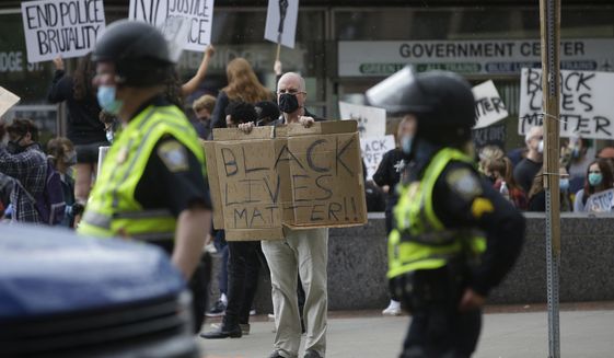 A protester holds a placard, center, as police walk through the street during a protest against police brutality, Sunday, June 7, 2020, in Boston, triggered by the death of George Floyd, an African American man who died on May 25 as a Minneapolis police officer pressed his knee into his neck, ignoring his cries and bystander shouts until he eventually stopped moving. (AP Photo/Steven Senne)