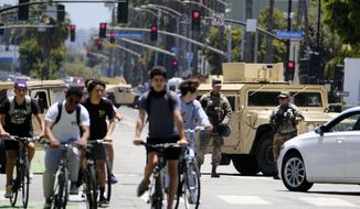 Cyclists ride down a street past a road block with National Guard troops along Ocean boulevard in Santa Monica, Calif. on Sunday June 7,2020.  Officials announced Sunday that National Guard troops will be pulled out of California cities where they&#39;ve been deployed for a week after rampant violence and thievery marred the first days of protests over the death of George Floyd. (AP Photo/Richard Vogel)