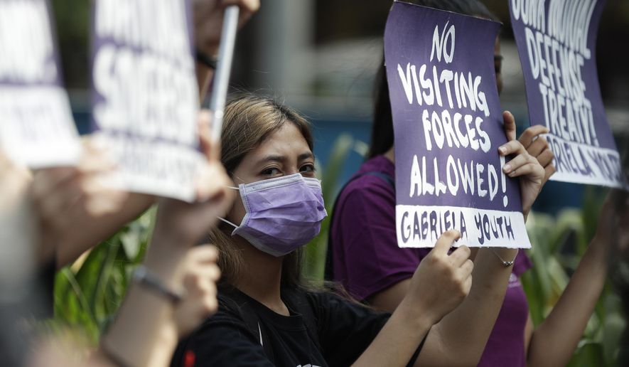 FILE - In this March 6, 2020, file photo, a woman protester wearing a protective mask holds a slogan during a rally outside the U.S. Embassy in Manila, Philippines against the planned military exercises between the Philippines and US under the Visiting Forces Agreement. The Philippines has decided not to suspend a defense pact with the U.S., avoiding a major blow to one of America’s oldest alliances in Asia.(AP Photo/Aaron Favila, File)