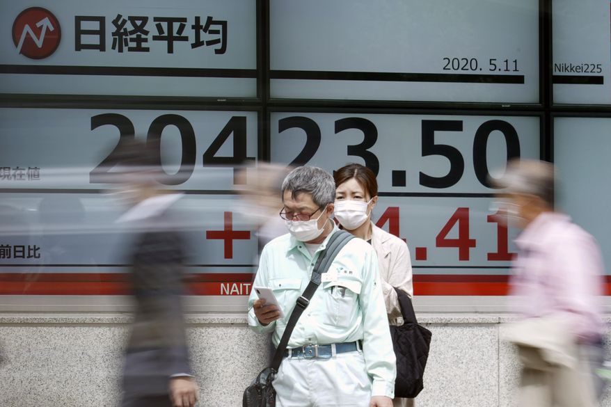 A man wearing a face mask to help curb the spread of the coronavirus stands as others walk past an electronic stock board showing Japan's Nikkei 225 index at a securities firm in Tokyo Monday, May 11, 2020. Shares advanced Monday, June 8, 2020 in Asia, buoyed by surprisingly strong U.S. jobs figures that helped power a surge on Wall Street on Friday. (AP Photo/Eugene Hoshiko)