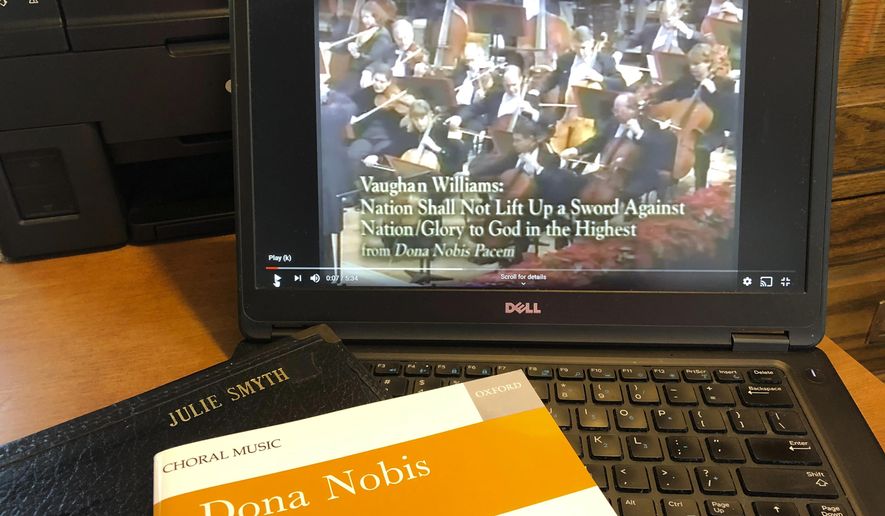 In this Monday, June 8, 2020, photo, a piece of music by Ralph Vaughan Williams is displayed in Worthington, Ohio, in front of a YouTube video of the Atlanta Symphony performing it. The coronavirus pandemic has forced choral singers to raise their single voices in song from isolated settings, singing to audio files or online videos rather than with other singers who have the potential of spreading COVID-19. (AP Photo/Julie Carr Smyth)