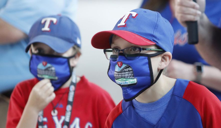FILE - In this June 1, 2020, file photo, Gavin Bollmer, left, and his buddy, Austin LaFountain, wear Globe Life Field masks as they tour the home of the Texas Rangers baseball team in Arlington, Texas. Many organizations are trying to bridge the budget gap from the coronovirus through enhanced sponsorship sales, such as temporary billboards that could be stretched over unsold sections of seats. Teams and leagues are selling branded face masks and other personal protective equipment. Almost all of them are trying to engage fans in new and creative ways. It won't come close to making up the budget shortfall, but the hope is to survive long enough for sports to return to normal. (AP Photo/LM Otero, File)