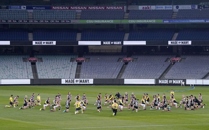 Australian Football League players from rivals Richmond and Collingwood teams, along with game officials, kneel before their game at the Melbourne Cricket Ground in Melbourne, Thursday, June 11, 2020, to show support for the Black Lives Matter movement. Aussie rules football is back after a three-month shutdown due to coronavirus restrictions. (Michael Dodge/AAP Image via AP)