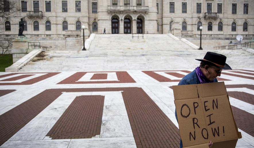 FILE - in this May 1, 2020 file photo, James Dunn stands outside the statehouse in Providence, R.I. with a handmade sign. The smallest U.S. state has the longest name, and it's not sitting well for some in the George Floyd era. Officially, Rhode Island was incorporated as "The State of Rhode Island and Providence Plantations" when it declared statehood in 1790. Now, opponents have revived an on-and-off effort to lop off the plantations reference, saying it evokes the dark legacy of slavery. (AP Photo/David Goldman, File)