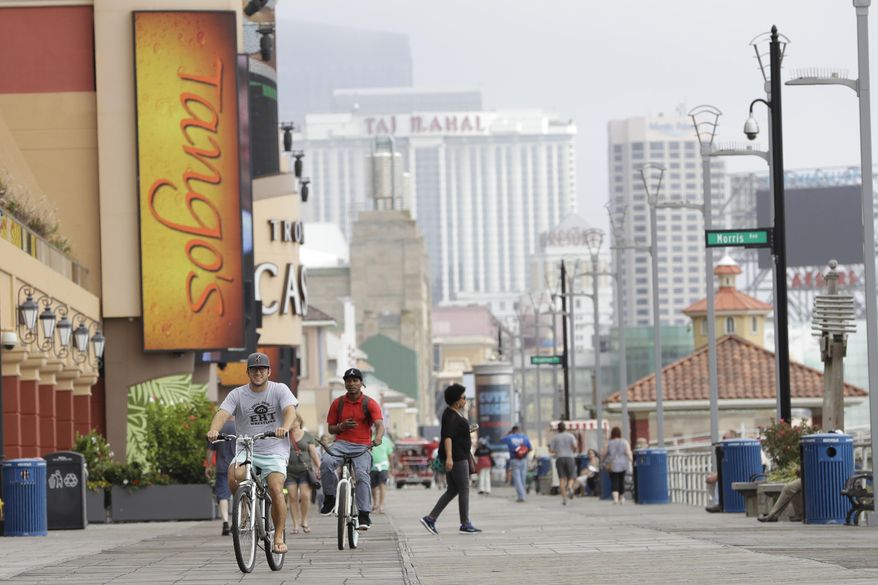 FILE - In this Sept. 27, 2017, file photo, casinos give backdrop as men ride bicycles along the boardwalk in Atlantic City, N.J. Many folks could use a drink right about now, and starting Friday  they’ll be able to do it while strolling the Atlantic City Boardwalk. Mayor Marty Small issued an executive order on Monday allowing for public consumption of alcohol in a few areas including the Boardwalk, the non-residential areas of Gardner's Basin, and some local streets just off the Boardwalk in an area known as the “Orange Loop” after the streets designated with orange markings in the Monopoly board game.   (AP Photo/Julio Cortez, File)