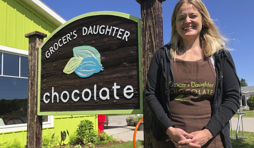 In this June 11, 2020 photo, Jody Hayden poses at the Grocer's Daughter chocolate shop which she owns with her husband in Empire, Mich, She said her family wears masks and keep their distance from others _ and will expect their customers to do the same when they open the doors to their shop, next Friday, June. 19. Even as states and metropolitan areas relax restrictions on social and economic life amid the ongoing coronavirus pandemic, a new poll finds that most Americans aren't ready to abandon behaviors that protect themselves and the people around them. (AP Photo/John Flesher)