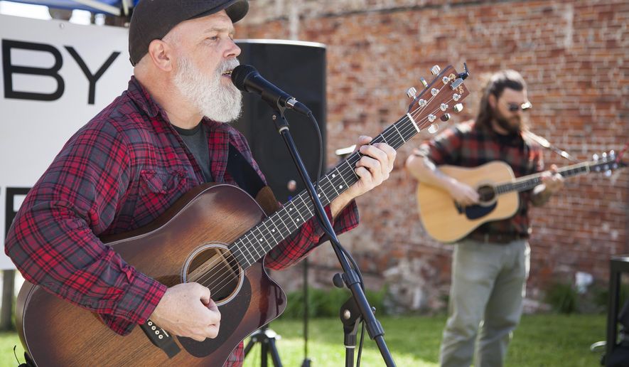 Joshua Grassle, left, and Jared Unfried perform a curbside concert outside Germania Brew Haus coffee shop in Alton, Ill., in May 2020. Although community art and entertainment has been largely absent the past few months due to social gathering limitations, Jacoby Arts Center has returned to the Alton stage with curbside art classes and concerts scheduled throughout the month of June in addition to a new art installation inside the center’s main gallery. (Jeanie Stephens/The Telegraph via AP)