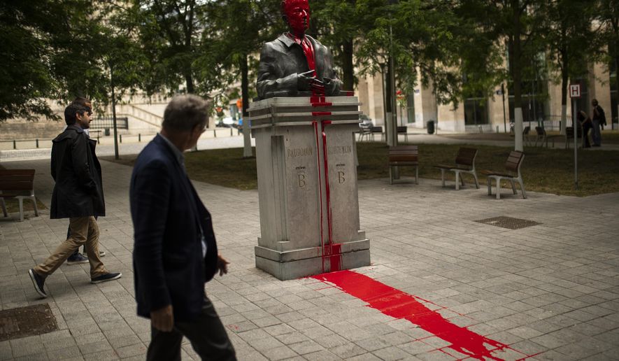 People walk past a bust of former Belgian King Baudouin in Brussels, Friday, June 12, 2020, vandalized as part of anti-racism protests in the country. (AP Photo/Francisco Seco)
