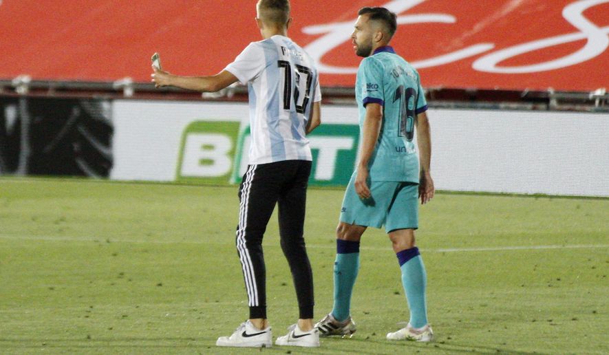 A supporter, left, invades the pitch and attempts to take a selfie with FC Barcelona's Jordi Alba during the Spanish La Liga soccer match between Mallorca and FC Barcelona at Son Moix Stadium in Palma de Mallorca, Spain, Saturday, June 13, 2020. With virtual crowds, daily matches and lots of testing for the coronavirus, soccer is coming back to Spain. The Spanish league resumes this week more than three months after it was suspended because of the COVID-19 pandemic. (AP Photo/Francisco Ubilla)