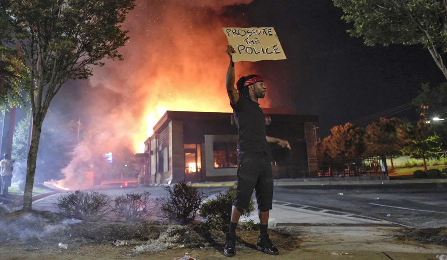 A person holds a sign as a Wendy&#x27;s restaurant burns Saturday, June 13, 2020, in Atlanta after demonstrators set it on fire. Demonstrators were protesting the death of Rayshard Brooks, a black man who was shot and killed by Atlanta police Friday evening following a struggle in the Wendy&#x27;s drive-thru line. (Ben GrayAtlanta Journal-Constitution via AP)