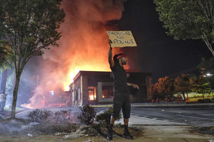 A person holds a sign as a Wendy&#x27;s restaurant burns Saturday, June 13, 2020, in Atlanta after demonstrators set it on fire. Demonstrators were protesting the death of Rayshard Brooks, a black man who was shot and killed by Atlanta police Friday evening following a struggle in the Wendy&#x27;s drive-thru line. (Ben GrayAtlanta Journal-Constitution via AP)