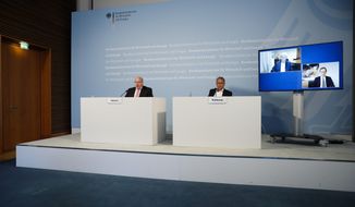 German Economy Minister Peter Altmaier, left, state secretary at the economic ministry Ulrich Nussbaum, right, attend a news conference with investor Dietmar Hopp, on the screen left, and CureVac CEO Franz-Werner Haas, on the screen right, at the economy ministry about the in Berlin, Monday, June 15, 2020. The German government is taking a 23 percent stake in the German company working on a potential vaccine for the coronavirus. (AP Photo/Markus Schreiber, Pool)