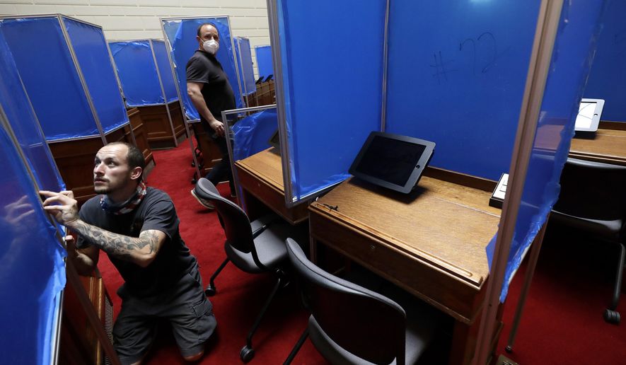 Worker Toby King, left, installs plastic partitions, with a removable blue protective covering, between desks, Monday, June 15, 2020, on the floor of the House Chamber at the Statehouse, in Providence, R.I. The partitions are being installed before the expected return of lawmakers to the Statehouse on Wednesday, June 17. (AP Photo/Steven Senne)
