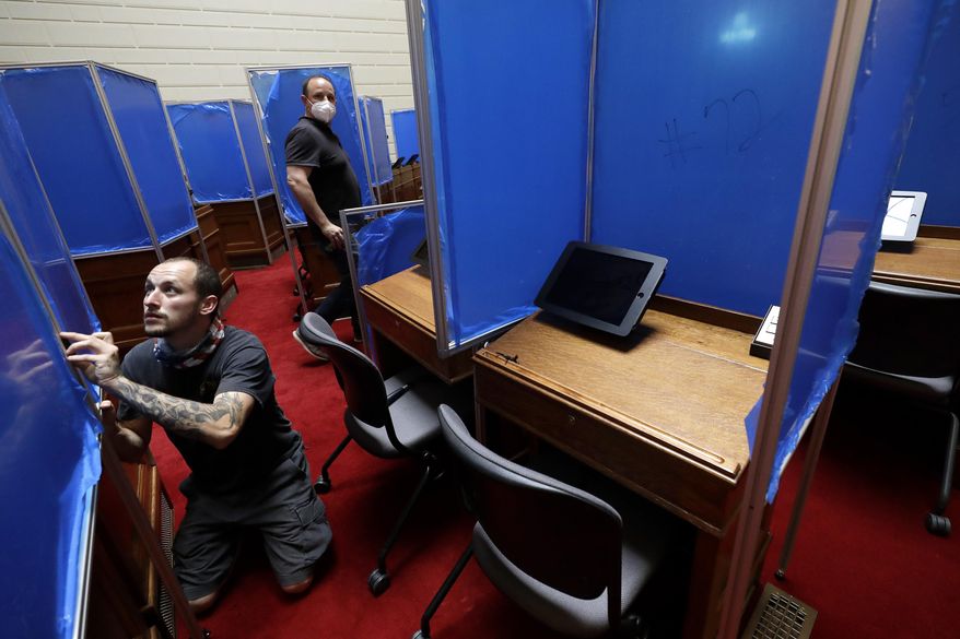 Worker Toby King, left, installs plastic partitions, with a removable blue protective covering, between desks, Monday, June 15, 2020, on the floor of the House Chamber at the Statehouse, in Providence, R.I. The partitions are being installed before the expected return of lawmakers to the Statehouse on Wednesday, June 17. (AP Photo/Steven Senne)