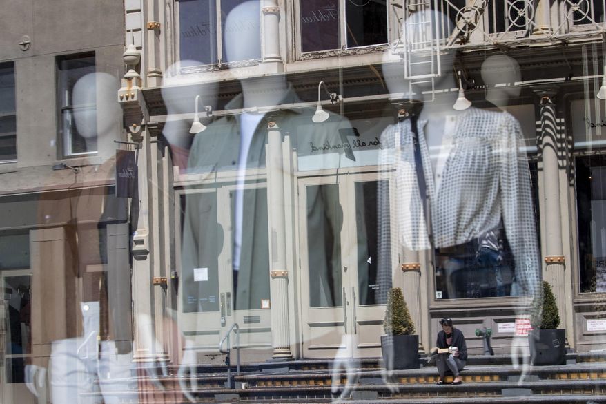In this May 7, 2020, file photo, a woman sitting on a stoop reading a book in the sun is seen reflected by a closed clothing store's window on West Broadway in the SoHo neighborhood of the Manhattan borough in New York. U.S. retail sales likely recovered somewhat in May as the economy increasingly reopened from closures caused by the coronavirus and more shoppers felt confident enough to spend. The Commerce Department is expected to report Tuesday, June 16, 2020, that retail purchases climbed 9% from April to May, according to economists surveyed by the data provider FactSet. (AP Photo/Mary Altaffer, file)