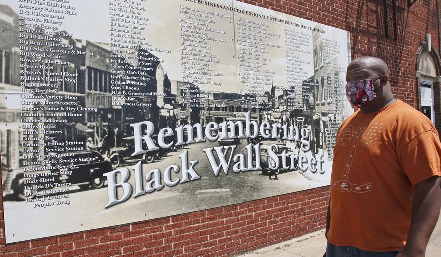 Freeman Culver stands in front of a mural listing the names of businesses destroyed during the Tulsa race massacre in Tulsa, Okla., Monday, June 15, 2020, on the other side of what's historically the city's white-black dividing line from where President Donald Trump will rally Saturday. (AP Photo/Sue Ogrocki)