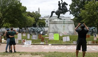 People visit Lafayette Park where protest signs are seen along the fencing that surrounds a statue of President Andrew Jackson, Tuesday, June 16, 2020, near the White House in Washington, where protests have occurred over the death of George Floyd, a black man who was in police custody in Minneapolis. (AP Photo/Jacquelyn Martin)
