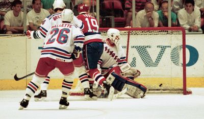 John Druce of the Washington Capitals (19), puts the puck past New York Rangers goalie John Vanbiesbrouck in overtime to win the NHL Patrick Division finals April 28, 1990, at Madison Square Garden. The Caps beat the Rangers 2-1, and won the series four games to one. Defending on the play is Rangers Troy Mallette (26), and Ron Greschne, upper left. (AP Photo/Ed Bailey)