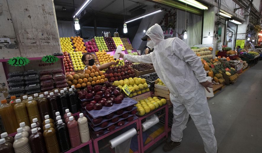 A health worker in protection gear to curb the spread of the new coronavirus gives alcohol to a vendor to disinfect her hands at the Central de Abasto market in Mexico City, Thursday, June 18, 2020. (AP Photo/Marco Ugarte)