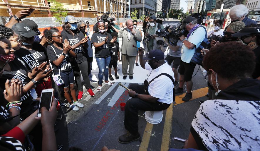 Artist Hubert Massey raises a fist after signing his "Power to the People" mural on Woodward Ave, Friday, June 19, 2020, in Detroit. The mural, funded by the Knight Foundation and Bedrock, spells out "Power to the People".(AP Photo/Carlos Osorio)