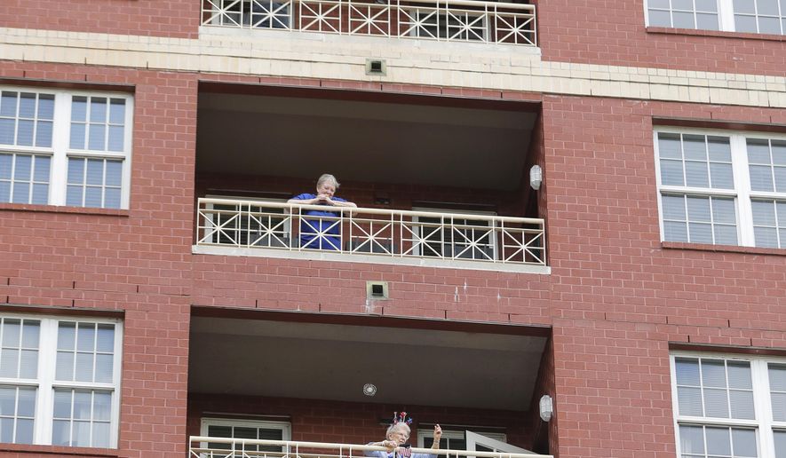 FILE - In this March 20, 2020, file photo, a resident of the Lambeth House, where a cluster of COVID-19 has formed, reacts from her balcony as opera singers Irini Hymel and Bryan Hymel sing to the quarantined residents in New Orleans. As coronavirus cases spike ever higher in Louisiana, the state's nursing homes, assisted living sites and adult residential care facilities are showing more and more "clusters" of the virus, but the full scale of the outbreak at those sites remains uncertain. (AP Photo/Gerald Herbert, File)