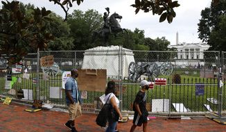 People wear face masks to protect against the spread of the new coronavirus as they walk past protest signs affixed to fencing surrounding a statue of President Andrew Jackson in Lafayette Park near the White House in Washington, Saturday, June 20, 2020. (AP Photo/Patrick Semansky)