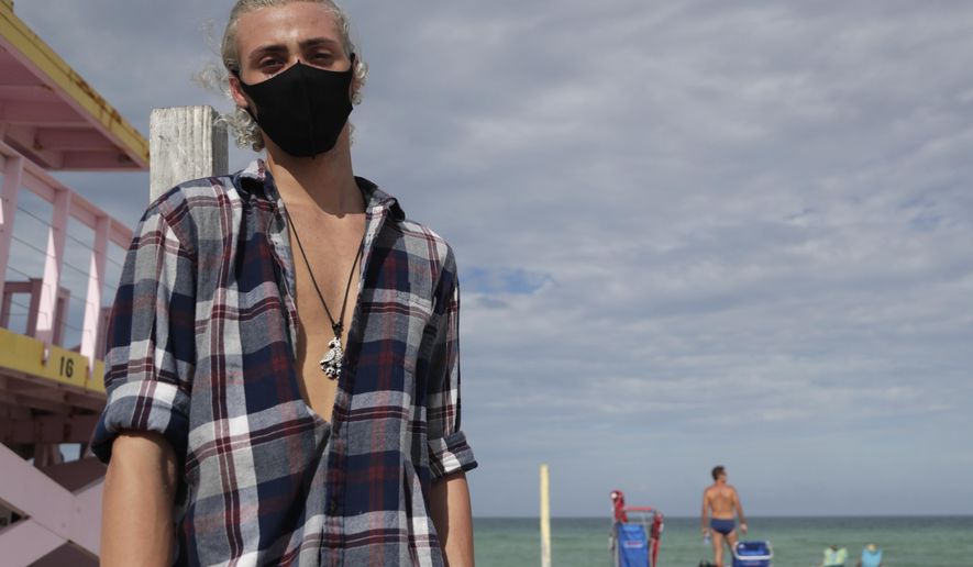 Nivek Divincci wears a protective mask as he poses for a photograph on the beach at Haulover Park during the new coronavirus pandemic, Friday, June 19, 2020, in Miami. Warm weather beach destinations are the most popular vacation searches, with Florida, Myrtle Beach, S.C., San Diego and Key West, Fla., among the top considerations. (AP Photo/Lynne Sladky)