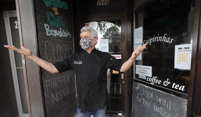 Owner Claudio Gianello stands in the doorway of his temporarily closed Café Beaudelaire restaurant, Tuesday, June 23, 2020, in Ames, Iowa. Within a few weeks of Gov. Kim Reynolds opening bars and restaurants to customers again two major college cities in Iowa are seeing spikes in coronavirus cases among young adults between 19 and 25. In Ames the surge is serious enough to prompt several owners of restaurants and bars near the Iowa State University campus to close voluntarily just weeks after reopening. (AP Photo/Charlie Neibergall)