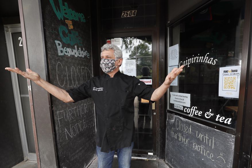 Owner Claudio Gianello stands in the doorway of his temporarily closed Café Beaudelaire restaurant, Tuesday, June 23, 2020, in Ames, Iowa. Within a few weeks of Gov. Kim Reynolds opening bars and restaurants to customers again two major college cities in Iowa are seeing spikes in coronavirus cases among young adults between 19 and 25. In Ames the surge is serious enough to prompt several owners of restaurants and bars near the Iowa State University campus to close voluntarily just weeks after reopening. (AP Photo/Charlie Neibergall)